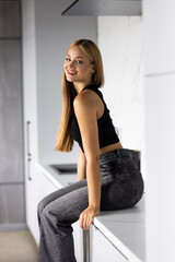Young woman looking at camera while sitting on the kitchen counter