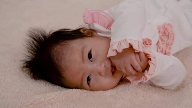 4K close-up photo of a 3-month-old Asian newborn playing in bed with a happy smile on her face. and wriggling with his mother's teasing Put your hand on your mouth and suck your fingers.