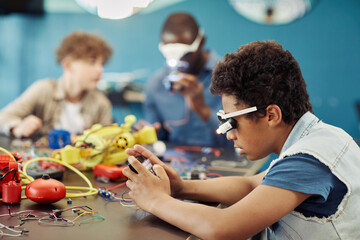 Side view portrait of young black boy building robots in engineering class at school, copy space