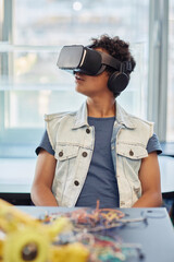 Vertical portrait of black teenage boy using VR technology in engineering class and looking around