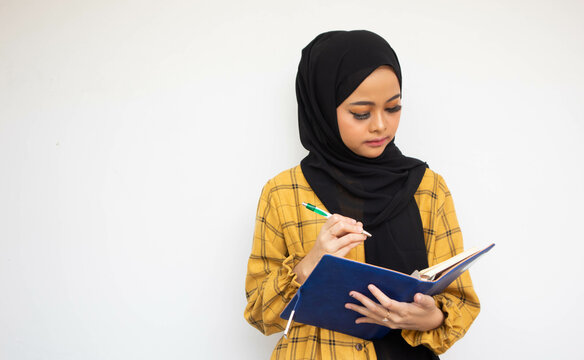 Portrait of a young woman hijab holds a book and pen to writing while thinking