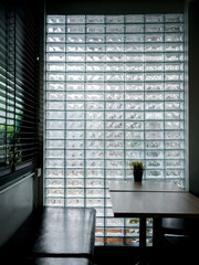 Glass brick wall background. Modern glass block wall with the light through decorated in the cafe with empty table and long seat, dim light room, vertical style. Interior decor space wall concept.