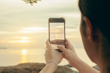 Asian women take photos and video calls at sea and beach in the morning at sunrise with their mobile phones, smartphones for posting to the internet online while traveling on vacation.