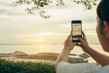 Asian women take photos and video calls at sea and beach in the morning at sunrise with their mobile phones, smartphones for posting to the internet online while traveling on vacation.