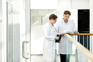 Obraz premium Minimal portrait of two expert doctors discussing case in hall of modern clinic in white tones, copy space