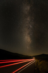 Long exposure traffic trails from tail lights stretching down the road toward the milky way