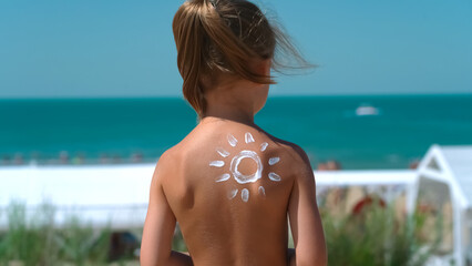 Little childs back with sunscreen or sunblock on background of hotel beach with blue sea. Skin care from sun. Concept of summer vacation, travel, holiday.