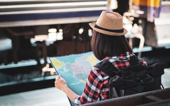 Young asian woman traveller is looking at the map at the train station, Travel and transportation concept. Traveler is waiting for her train. Outdoor adventure travel by train concept.
