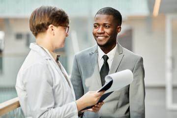 Waist up portrait of smiling African American businessman talking to female colleague in hall of office building