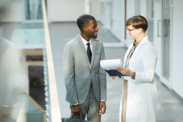 High angle portrait of smiling African American businessman talking to female colleague in hall of...