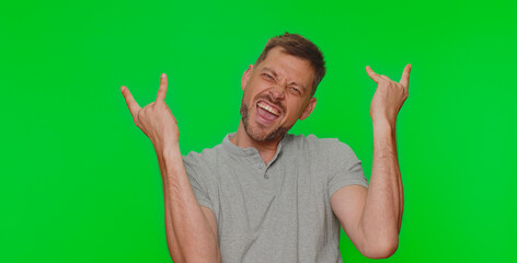 Overjoyed delighted handsome man showing rock n roll gesture by hands, cool sign, shouting yeah with crazy expression, dancing, emotionally rejoicing in success. Adult guy on chroma key background