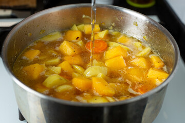 Water is poured into a saucepan with fried vegetables to make pumpkin soup