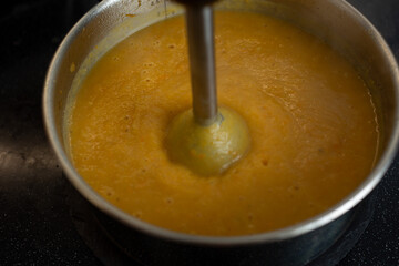 In a saucepan with an immersion blender, cooked vegetables are interrupted in a soup puree