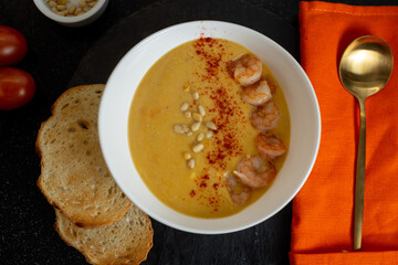 Pumpkin soup garnished with shrimp, paprika and pine nuts with two toasted toasts