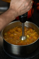 In a saucepan with an immersion blender, cooked vegetables are interrupted in a soup puree