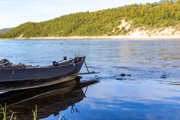Naklejka na ściany i meble A wooden fishing boat in the Teno river in Lapland, Finland, with white sand and forest on the opposite bank in the background. Teno has been praised as one of the best salmon rivers in Europe.