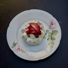 Pavlova desert with slices of vine peaches and 2 pink flowers on an beautiful old porcelain plate