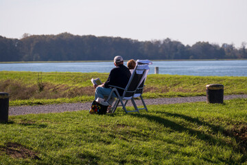 Ein älteres Paar sitzt auf Stühlen am Rheinufer in der Sonne