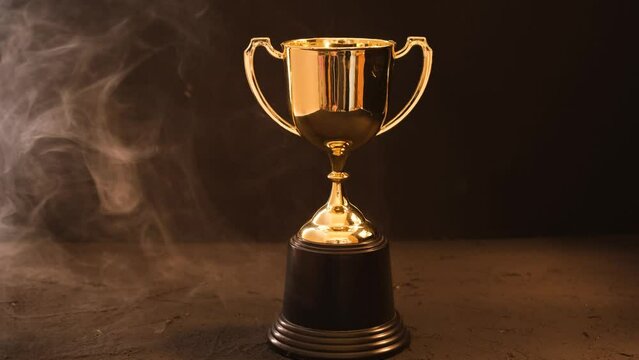 The golden trophy on a black background with smokes around a fierce and fiery concept of competition or victory.