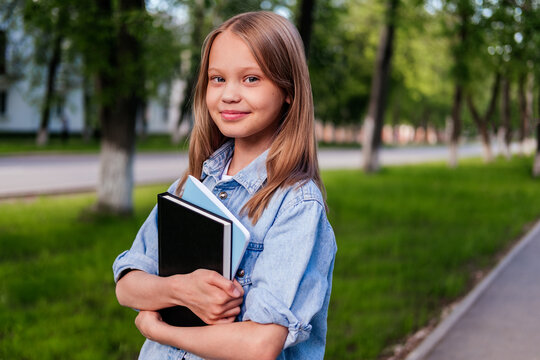 Smiling girl standing on street and holding notebooks. Child outdoor. Back to school concept