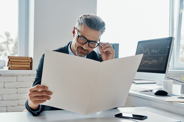 Handsome mature man in formalwear going through the documents while sitting in office