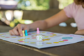 Board game and kids leisure concept - little girl hold figure in hand. yellow, blue, pink chips in children play.Table game. Movement. The girl moves the chip. Victory.
