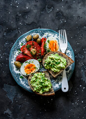 Fototapeta na wymiar Delicious breakfast, snack, tapas - avocado sandwiches, boiled egg, fresh ripe tomatoes on a dark background, top view