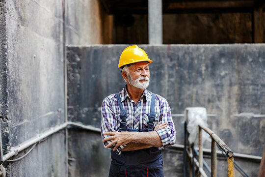 Heavy industry and industry operating. A senior supervisor standing in a metal construction facility with arms crossed and looking away.