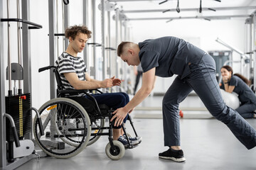 Fototapeta na wymiar Rehabilitation specialist helps a guy in a wheelchair to do exercise on decompression simulator for recovery from injury. Concept of physical therapy for people with disabilities