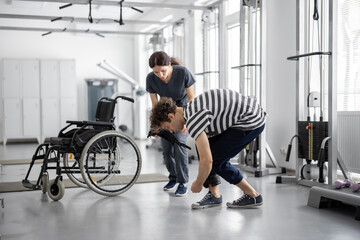 Guy wears cuffs on his legs in preparation for exercise, nurse with wheelchair on the background....