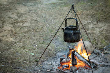 Campfire with cooking food in a saucepan on a tripod. Cooking on fire, camping cooking. Living in tents in the fresh air. Campfire at the campsite. Camping food, cooking on an open fire. Copy space