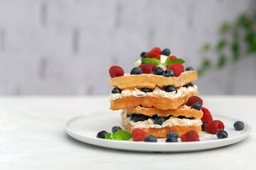 Fresh Viennese or Belgian waffles on a plate with fresh raspberries and blueberries and whipped cream.