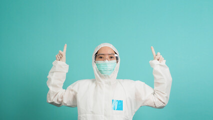 Asian woman in PPE suit wears face mask is pointing fingers up on green or Tiffany Blue backgrounds.