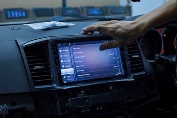 A cropped hand adjusting the in-car display system. Noise and luminance are visible due to low light and high ISO