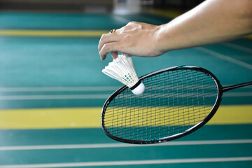 Badminton racket and old white shuttlecock holding in hands of player while serving it over the net ahead, blur badminton court background and selective focus