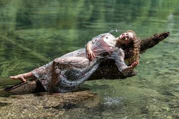 A young model plays with splashes on a mountain lake against the background of crystal clear transparent water
