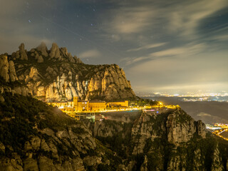 Paisaje nocturno de la montaña de Montserrat con fondo iluminado de poblaciones y cruz en primer termino en Cataluña (España).