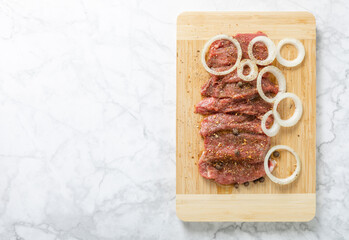 Raw beef with onions marinated with spices on light texture background.Meat cooking recipe.Juicy steak on a bamboo board, close-up. Place for text, space for copy.
