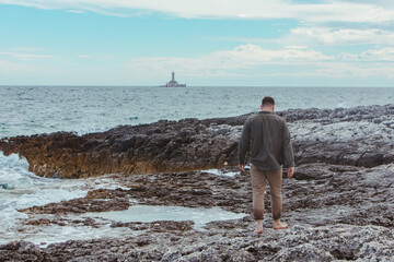 young adult man walking by rocky sea beach barefoot summer vacation