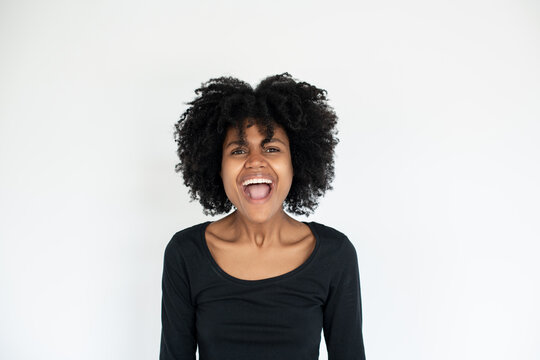 Portrait of excited African American woman laughing. Young female model wearing black dress looking at camera and shouting against white background. Excitement and happiness concept