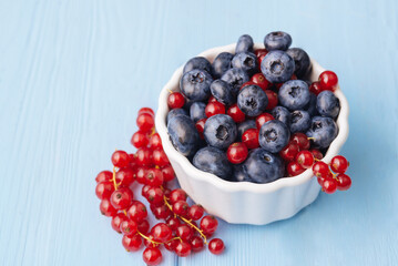 Assorted berries in white bowl on wood: blueberry and red currant on blue wood background. Summer Freshly Berry