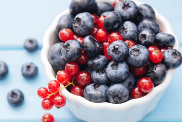 Assorted berries in white bowl on wood: blueberry and red currant on blue wood background. Summer Freshly Berry