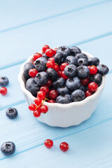 Assorted berries in white bowl on wood: blueberry and red currant on blue wood background. Summer Freshly Berry