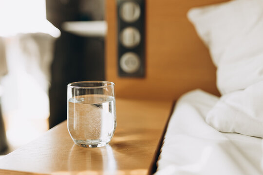 Glass of water on wooden table bokeh background. Good habit - drinking a glass of water before going to sleep. Modern and comfortable home or hotel bedroom interior