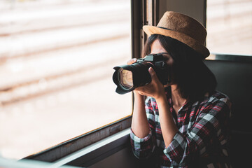 Tourist woman taking a photo with camera of side of train on railway background. Young asian woman traveler with backpack in the railway, Travel concept