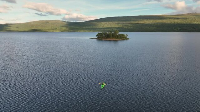 Scenic fly away video above women in green kayak paddling from small island in blue lake in Scandinavian mountains. Sweden, Norway