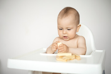 A cute little baby sits in a high chair and plays educational games. wooden construction set. Ecological. A light background, a place for text.