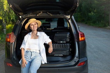 Car journey. A young beautiful woman in a hat on vacation rests near the car. Lifestyle