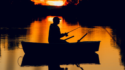 Fishermen in a boat with a fishing rod in hands in the setting sun. Silhouette of a fisherman