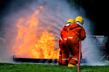 Naklejka premium Firefighter Concept. Fireman using water and extinguisher to fighting with fire flame. firefighters fighting a fire with a hose and water during a firefighting training exercise 
